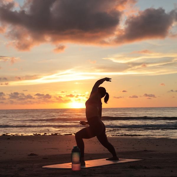Silhouette of a person doing a balancing yoga pose against a warm sunrise.